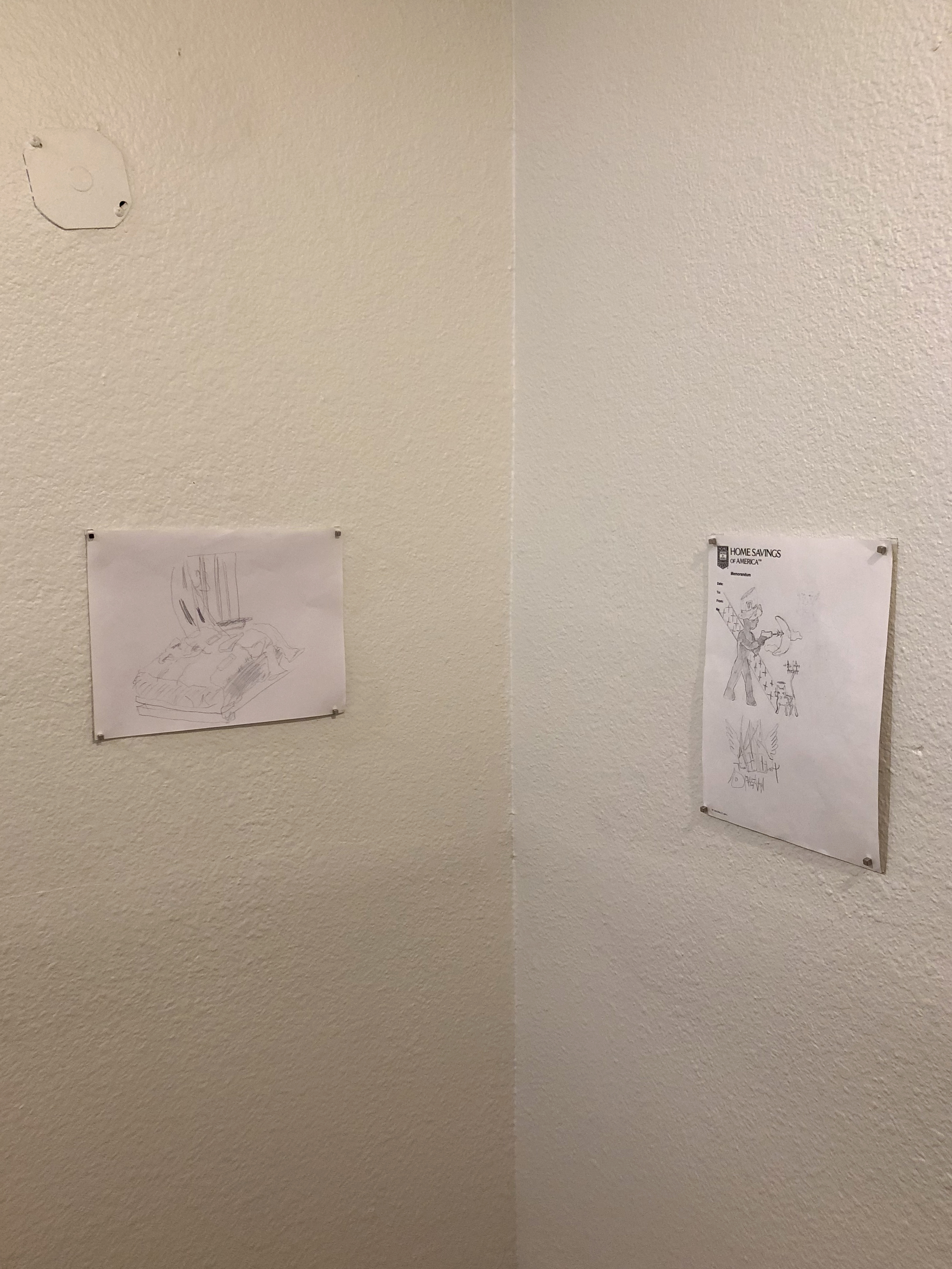 Two small drawings hung on two white walls that form a corner